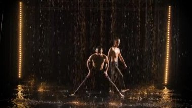 Yağmurda iki akrobatın performansı. Erkekler amuda kalkarlar ve ağır çekimde denge kurarlar..