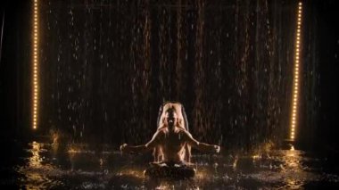 Yağmurda heyecan verici bir akrobatik gösteri. Siyah bir stüdyonun arka planında poz veren üç adam ağır çekimde arka planda..