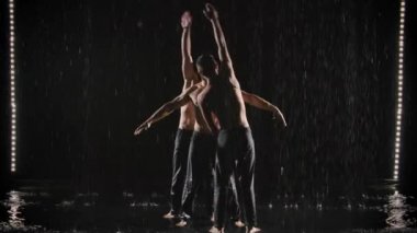 Üç akrobat su derelerinin altında denge pozu veriyor. Atletik adamlar takım çalışmasında zor numaralar yapıyorlar. Yavaş çekim.