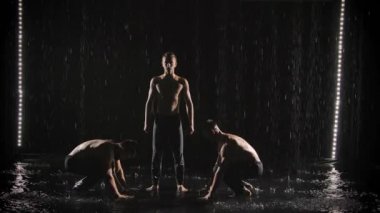 Üç akrobat su derelerinin altında denge pozu veriyor. Atletik adamlar takım çalışmasında zor numaralar yapıyorlar. Yavaş çekim.