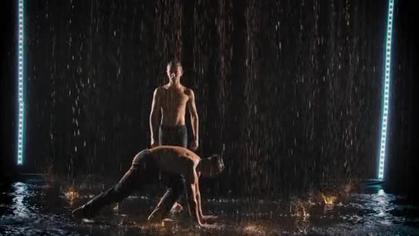 雨の中で2人のアクロバットによるパフォーマンス。男はスローモーションで手とバランスを行う. — ストック動画