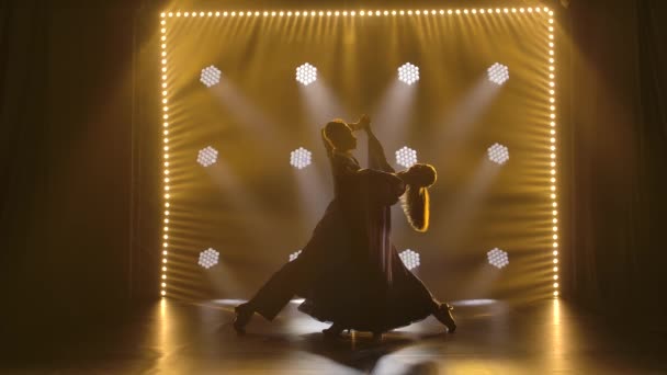 Un par de bailarines de salón profesionales bailando un vals en un estudio oscuro en el centro de atención. Movimiento lento. — Vídeo de stock