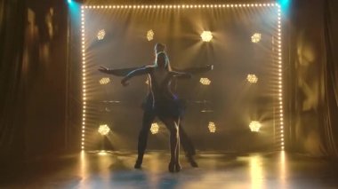 İki genç balo dansçısı tutkulu Latin Amerika dansları yapıyor. Dumanlı arka planda sarı ışıklı iki dansçının siluetleri. Yavaş çekim.