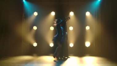 Genç çift tutkuyla rumba yapıyor ve arka planda sarı spot ışıklarıyla stüdyoya taşınıyorlar. Yavaş çekim.