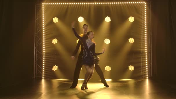 Jeune couple dansant passionnément la rumba et se déplaçant dans le studio avec des projecteurs jaunes en arrière-plan. Mouvement lent. — Video