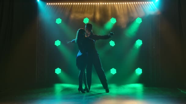 Un par de bailarines profesionales realizan elementos de bailes de salón latinoamericanos rumba, cha cha cha, samba. Siluetas pareja bailando apasionadamente en un estudio oscuro con luces verdes. Movimiento lento. — Vídeos de Stock