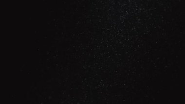 Siyah arka planda ince tozun panoramik hareketi. Parlak toz parçacıkları havada yüzer ve boşluğu doldurur. Kapatın. Yavaş çekim.
