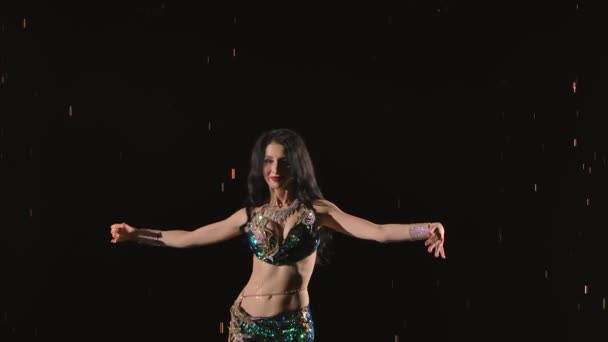 Among the raindrops, a woman in an exotic costume performs a belly dance and moves with a half naked body. Slow motion on black background close up. — Stock Video