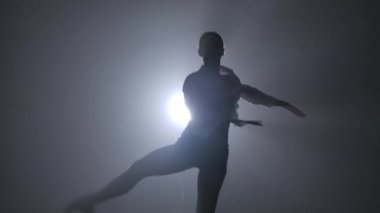 Koyu dumanlı bir stüdyoda kadın bir balerin tarafından sahnelenen Pirouette. Spot ışıkları altında siluetler. Ağır çekimde kapat..