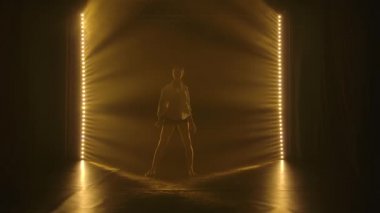 Genç, narin bir balerin modern, çağdaş bir bale dansında duygusal olarak dans ediyor. Sarı ışık ve dumanla karanlık bir stüdyoda çekildi. Siluet. Yavaş çekim.