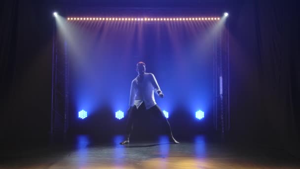 Zeitgenössisches Ballett, ein Mann führt Elemente moderner Choreographie auf und springt ins Rampenlicht. Silhouetten eines männlichen Tänzers in einem dunklen Studio. Zeitlupe. — Stockvideo