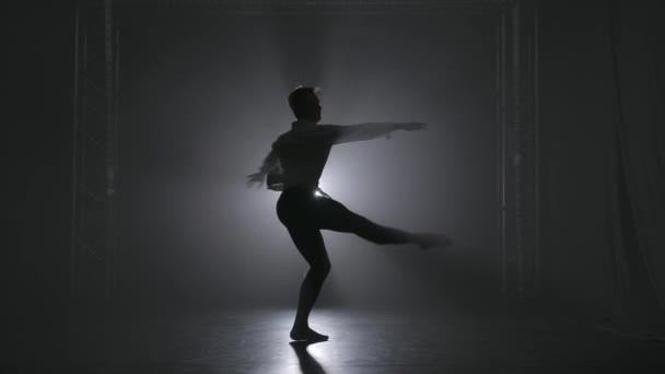 Piruet w wykonaniu młodego utalentowanego tancerza baletowego. Sylwetka w świetle reflektorów na dymiącym tle. Zwolniony ruch. — Wideo stockowe