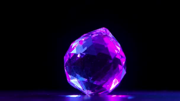 Un gran diamante multifacético gira sobre un fondo negro. Las facetas de la piedra brillan y brillan en los rayos violetas de luz, creando resplandor. En cámara lenta. De cerca.. — Vídeos de Stock