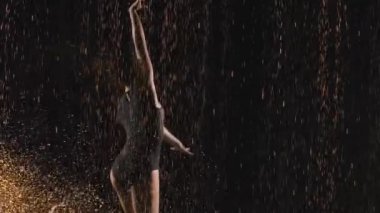 Jimnastikçi, yağmur damlaları ve su damlaları arasında akrobatik egzersizler yapan harika bir dans sergiliyor. Siyah arka planda bir siluet. Ağır çekimde kapat..