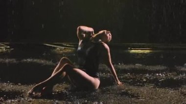 İnce bir jimnastikçi tarafından yapılan akrobatik elementlerle yapılan zarif bir dans yağmur ve su akıntıları altında. Kapatın. Yavaş çekim.