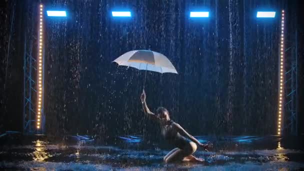 Αθλητικός γυμναστής επιδεικνύει στοιχεία ρυθμικής γυμναστικής με ομπρέλα κάτω από ρυάκια νερού. Πυροβολήθηκε σε σκούρο φόντο με μπλε φως σε αργή κίνηση. — Αρχείο Βίντεο