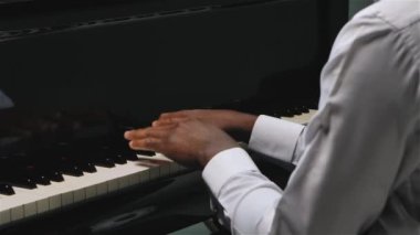 Afro-Amerikalı bir adam iki eliyle büyük piyanoda hafif klasik müzik çalar. Müzisyen elleri yavaş çekimde kapanır..