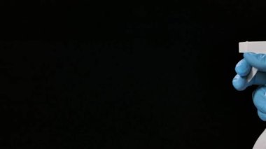 Koruyucu eldivenli bir adam dezenfeksiyon ve COVID 19 'un önlenmesi için temizlik spreyi sıkar. Siyah arka planda ince sıçramalar, yavaş çekimde yakın çekim..