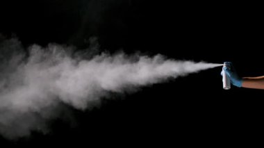 Koruyucu bir eldiven veren bir adam siyah arka plana dezenfekte spreyi sıkar. Koronovirüs koruma ve önleme. Bir salgını önlemek için. Ağır çekim. Kapat..