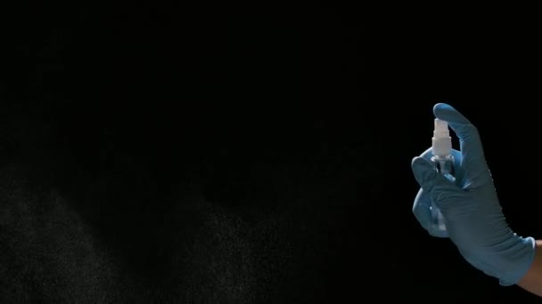 Una mano in un guanto protettivo azzurro spruzza un antisettico su uno sfondo nero. Spray disinfezione, protezione e prevenzione del COVID 19. Il concetto di servizi igienici. Vista laterale da vicino. Rallentatore. — Video Stock