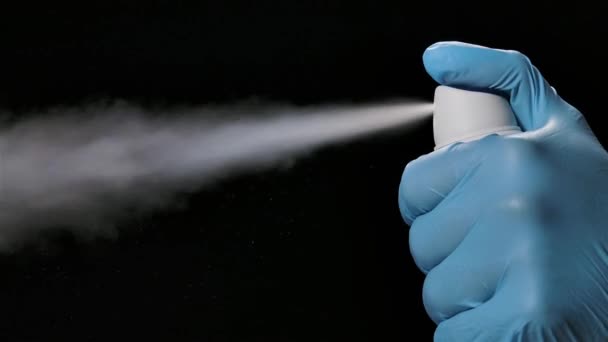Eine Hand in einem Schutzhandschuh sprüht ein desinfizierendes Spray. Prävention von COVID 19 und das Konzept der Hygiene. Zeitlupe Nahaufnahme auf schwarzem Hintergrund. — Stockvideo