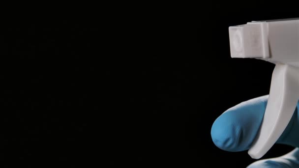 Un hombre con un guante protector salpica un spray antibacteriano sobre un fondo negro. Limpieza de superficies y desinfección de cerca. Prevenir la propagación del coronavirus. Movimiento lento. — Vídeos de Stock