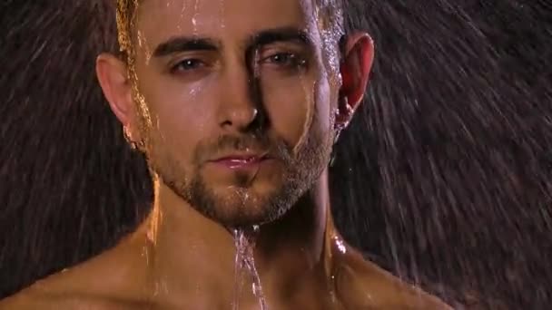 Porträt eines sexy jungen Mannes unter Duschdüsen, der erotisch in die Kamera blickt. Wasser fließt über sein Gesicht und erzeugt in Zeitlupe Wasserspritzer auf schwarzem Hintergrund. Nahaufnahme. — Stockvideo