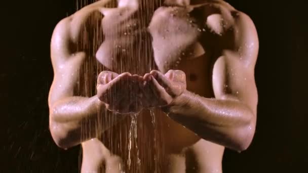 Sportig man tar en dusch i slow motion på en svart studio bakgrund. Närbild av muskulös bål av en hane som njuter av vattendroppar på armarna. suddig bakgrund. — Stockvideo