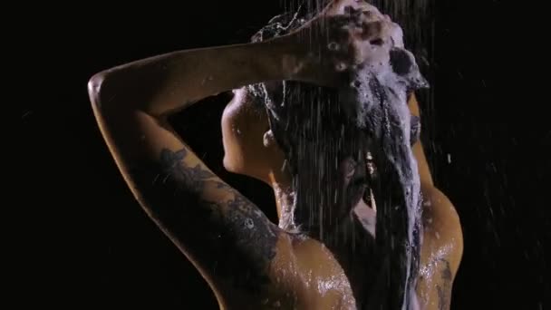 Nasse Brünette wäscht den Schaum von ihren Haaren ab, während sie in Zeitlupe unter einer warmen Dusche steht. Sexy Körper Nahaufnahme Rückansicht. — Stockvideo