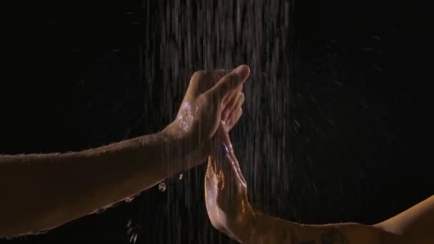 De sensuele aanraking van twee delicate palmen vingers man en vrouw in de douche onder stromend water. close-up in slow motion op een zwarte achtergrond. — Stockvideo