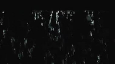 Karanlık bir stüdyoda gölgeliğin kenarından damlayan yağmur damlaları. Damlalar su püskürtülerine dönüşür ve yavaş çekimde aşağı akar. Sığınaktan vurulmuş, geçmişi bulanık. Kapat..