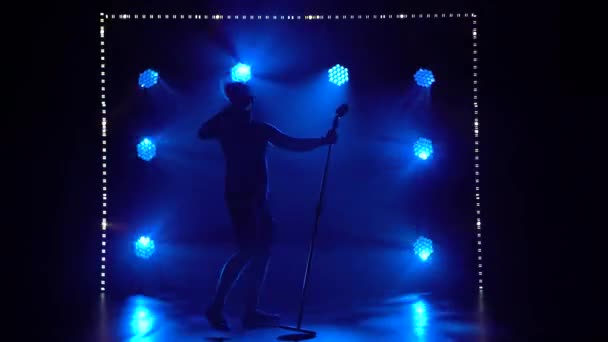 남성 가수가 어두운 스튜디오에서 역동적 인 푸른 빛을 내며 공연 한다. 마이크에 락을 생생하게 노래하고 있어요. 실루엣. — 비디오