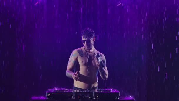 Ein sexy männlicher DJ mit einem glänzenden Körper aus dem Regen spielt auf der Fernbedienung, um in einem dunklen Studio Musik zu mischen. Finger berühren die Schieberegler, spielen an Deck elektronische Musik ab. Nahaufnahme in Zeitlupe. — Stockvideo