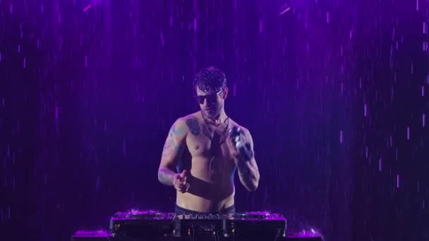 Un sexy dj masculino con un cuerpo brillante de la lluvia juega en el control remoto para mezclar música en un estudio oscuro. Los dedos tocan los controles deslizantes, tocan música electrónica en la cubierta. Primer plano en cámara lenta. — Vídeos de Stock