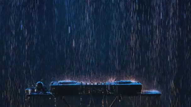 Consola de control de sonido DJ para mezclar música dance y auriculares bajo la lluvia sobre el fondo de un estudio oscuro con contraluz. De cerca. Movimiento lento. — Vídeos de Stock