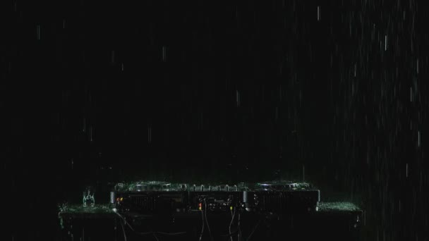 DJ-Tonregler zum Mixen von Tanzmusik und Kopfhörern im strömenden Regen auf dem Hintergrund eines dunklen Studios mit Hintergrundbeleuchtung. Aus nächster Nähe. Zeitlupe. — Stockvideo