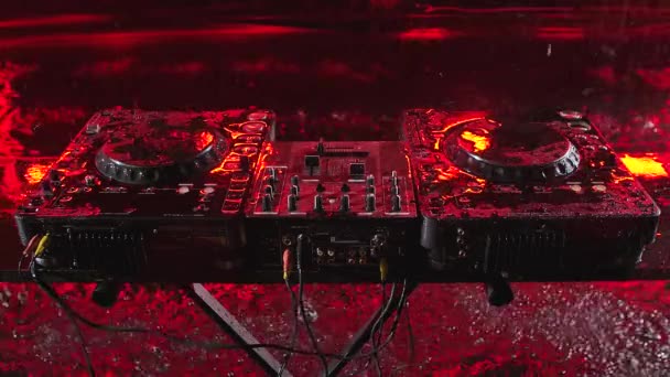 Controlador de mezcla de audio se encuentra en un estudio oscuro con iluminación roja. Herramientas DJ en la lluvia torrencial. Vista superior. De cerca. Movimiento lento. — Vídeos de Stock