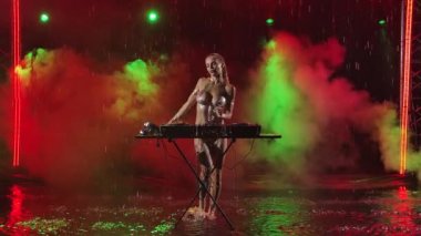 Karanlık stüdyoda canlı performans, seksi bayan DJ 'in dumanı ve neon ışıkları. Sarışın müzikten ve yağmurda dans etmekten hoşlanıyor. Yavaş çekim.