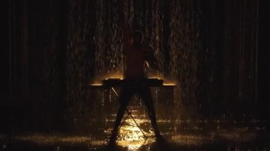 Çıplak gövdeli bir DJ pikaplarda elektronik dans müziği çalar ve karanlık bir stüdyoda yağmurdan zevk alır. Yavaş çekimde karanlık bir arkaplan karşısında video çekmek.