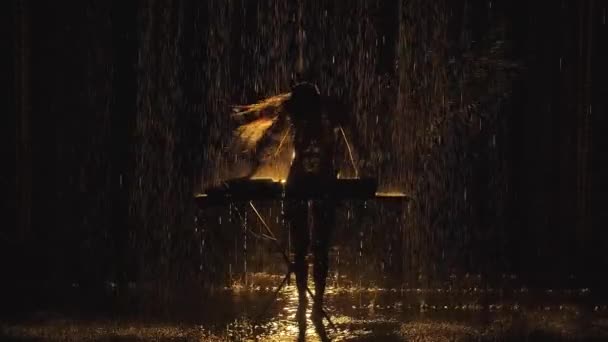 ボディーペイントに覆われた豪華なボディを持つ裸の女性がシルエットになり、ターンテーブルで電子ダンスミュージックを演奏し、雨滴の下で暗いスタジオで踊ります。スローモーション. — ストック動画