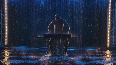Çekici erkek DJ dans ediyor ve mavi ışıklarla karanlık bir stüdyoda müzik çalıyor. Çıplak gövdeli, yağmur damlalarında parlayan bir adamın silueti. Yavaş çekim.