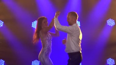 Esnek ve şehvetli dansçılar arka planda mavi spot ışıkları olan karanlık bir salonda dans ediyorlar. Latin dansı. Salsa olsun. Bachata. Ağır çekim. Kapat..