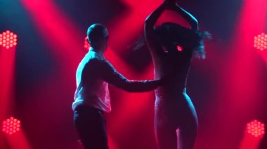Arka planda kırmızı ışıklar olan karanlık dumanlı bir stüdyoda dans eden bir çift salsa yapar. Beyaz gömlekli bir adam ortağıyla el ele tutuşuyor. Ağır çekim. Kapat..
