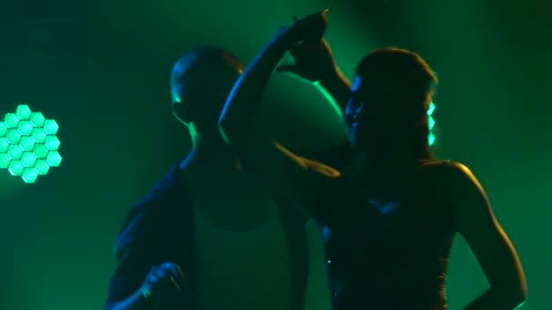 Silhouetten van salsa professionals. Een jonge man in het zwart danst met een mooie vrouw in een glimmende korte jurk. Rook in de studio. Dynamische veelkleurige neonlichten. Langzame beweging. Sluiten.. — Stockvideo