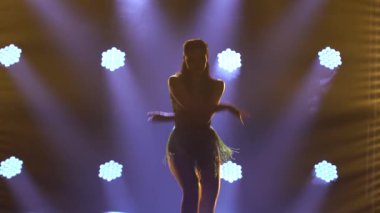 Kısa yanardöner elbiseli tutkulu bir bayan dansçı spot ışıklarında salsa yapıyor. Kalçalarını erotik bir şekilde hareket ettiren yanık bir esmerin siluetini kapat..