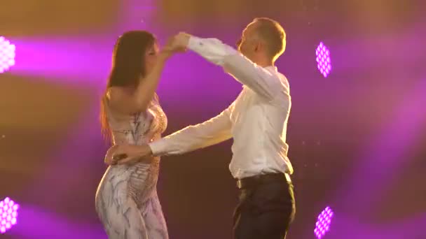 Jonge man en vrouw dansen hartstochtelijk hete mooie dans salsa. Een paar dansen in de studio tegen een achtergrond van paarse lichten. Sluiten.. — Stockvideo