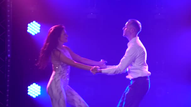 Krásná dvojice profesionálních umělců tancujících vášnivý salsa tanec. Mladý pár taneční prvky samba, rumba, salsa, bachata, tango v tmavém studiu v paprscích modrých světel. Zavřít. — Stock video