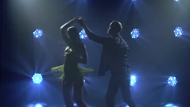 Bailarines hábiles bailan salsa en un estudio ahumado oscuro con luces azules. Siluetas de una sensual pareja realizando un baile latino artístico y emocional. De cerca.. — Vídeos de Stock