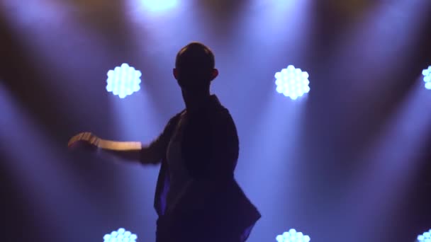 Homem atraente dançando dança salsa latino-americana cercada por fumaça e luzes de estúdio. Silhueta de um dançarino em roupas pretas de perto. — Vídeo de Stock