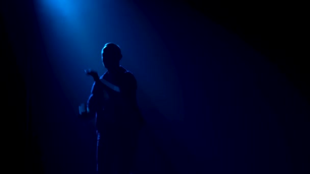 Muž středního věku tančí latinskoamerickou salsu obklopenou kouřem a studiovými modrými světly. Silueta tanečnice v černém oblečení zblízka. — Stock video
